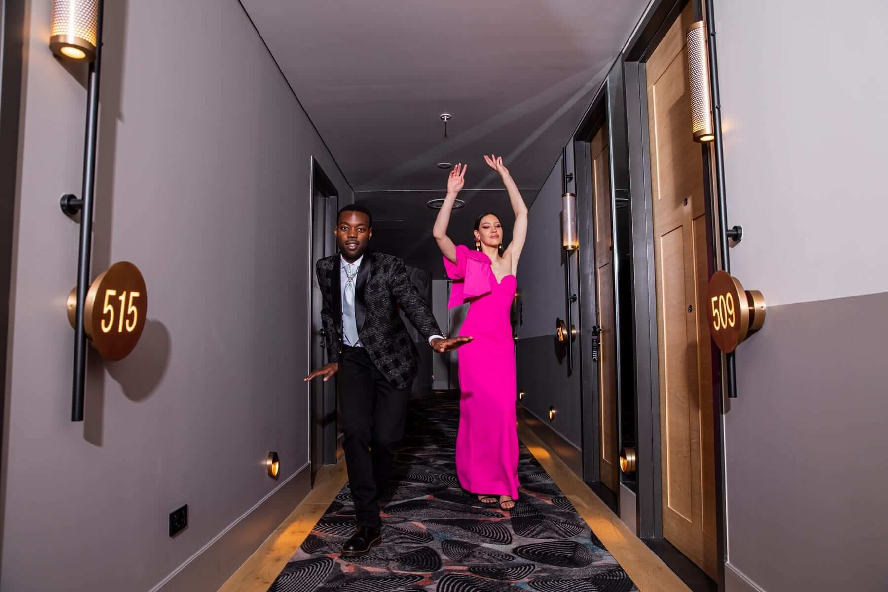 Two guests in evening wear dance down a hotel corridor
