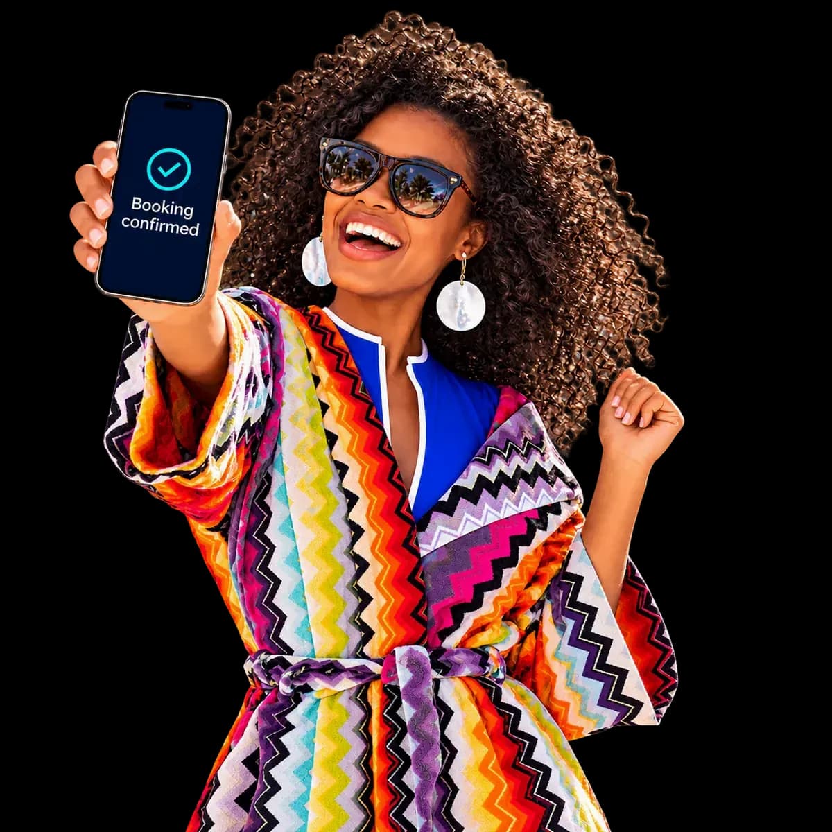 A delighted guest in a colourful robe holds up her phone, showing “Booking confirmed”